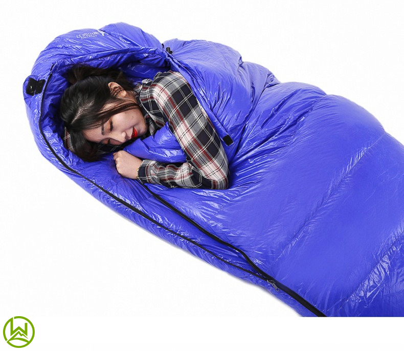 A camper comfortably nestled inside a cozy blue sleeping bag featuring a built-in hood, providing extra warmth and protection against the elements while enjoying the great outdoors.